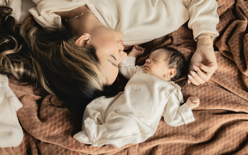 Mutter liegt mit Baby im Bett gegeneinander auf brauner Decke und der Kopf ist zum Kind hinblickend, Reiki in Niedernberg bei Aschaffenburg, Elke Maria Becker, Reiki Meisterin und Lehrerin